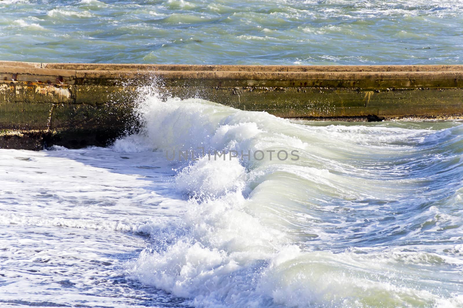 Sea waves with foam are breaking on the breakwater