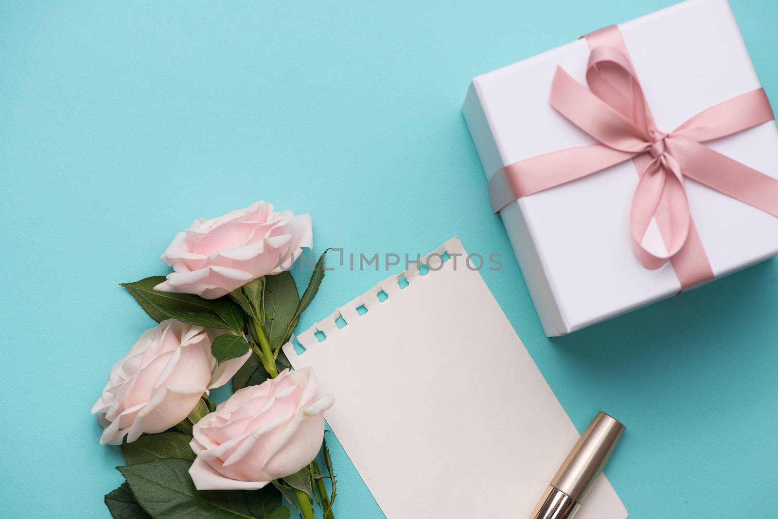 Mother's Day concept. Bouquet of pink roses with gift box and lipstick. Blank paper note for copy space.