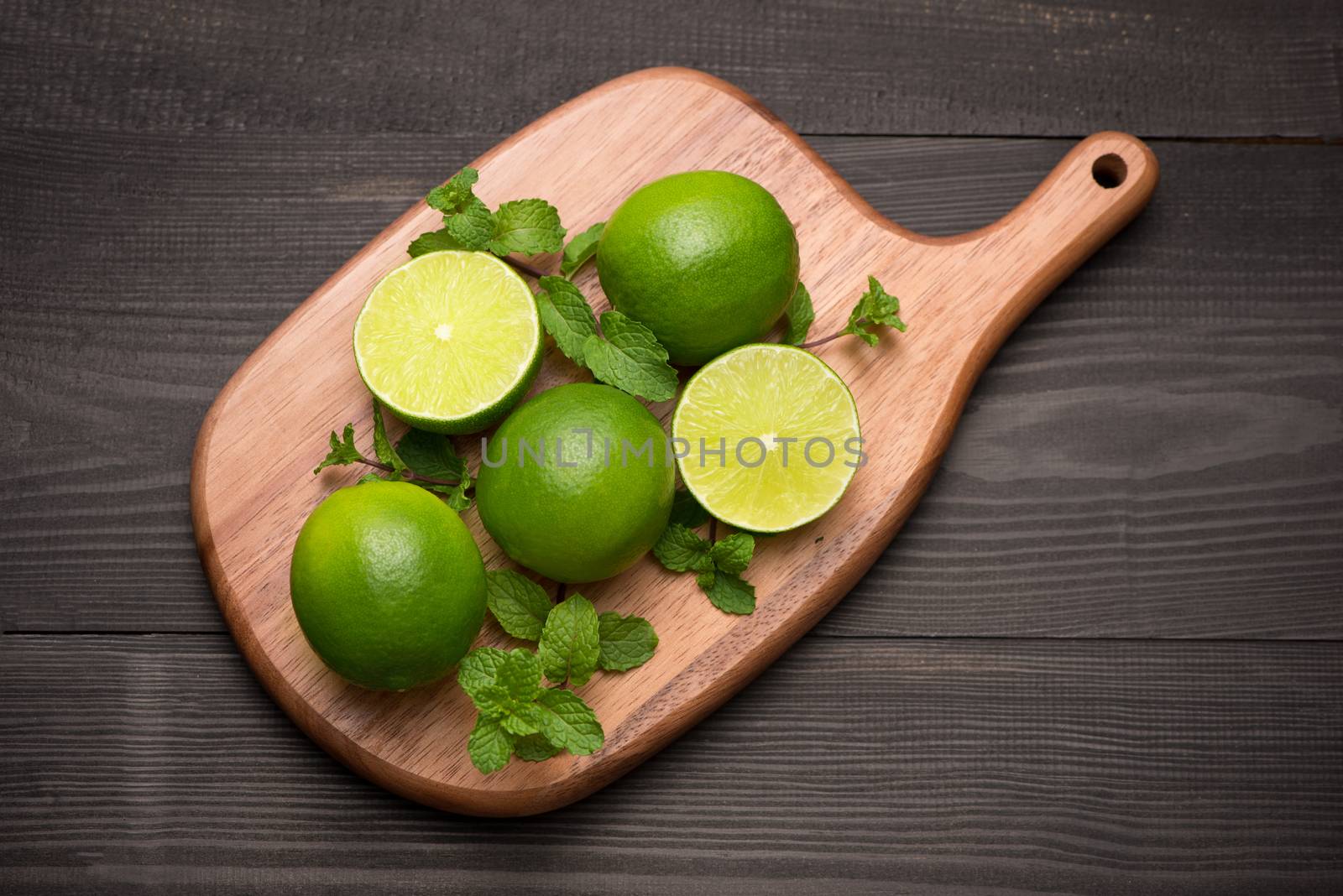 Fresh limes on cutting board on wooden table. Top view, background.