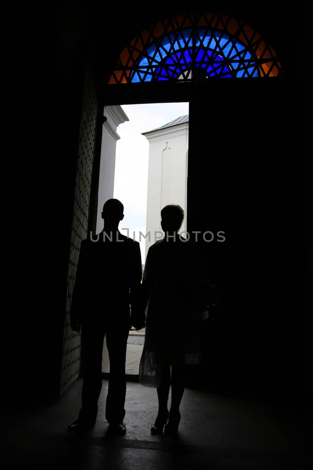 Romantic silhouette newlyweds are holding hands in the doorway of the church