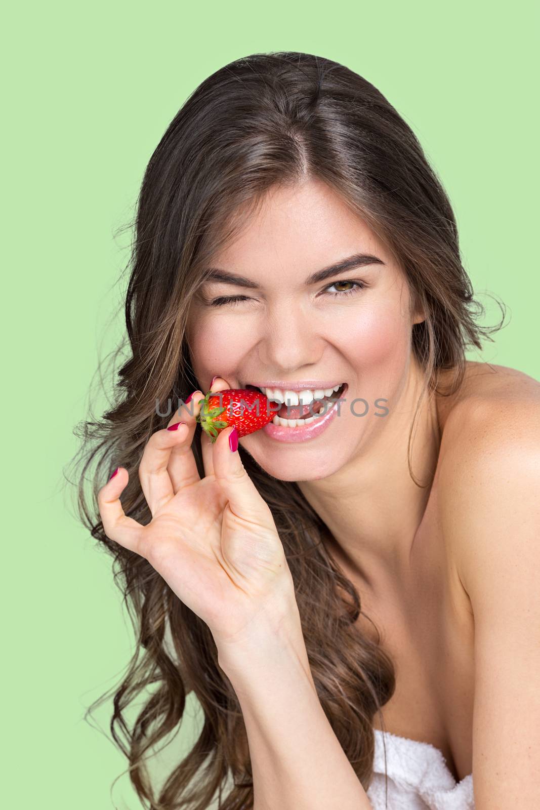 Studio portrait of a pretty girl with wavy fair hair and natural make-up eating strawberry