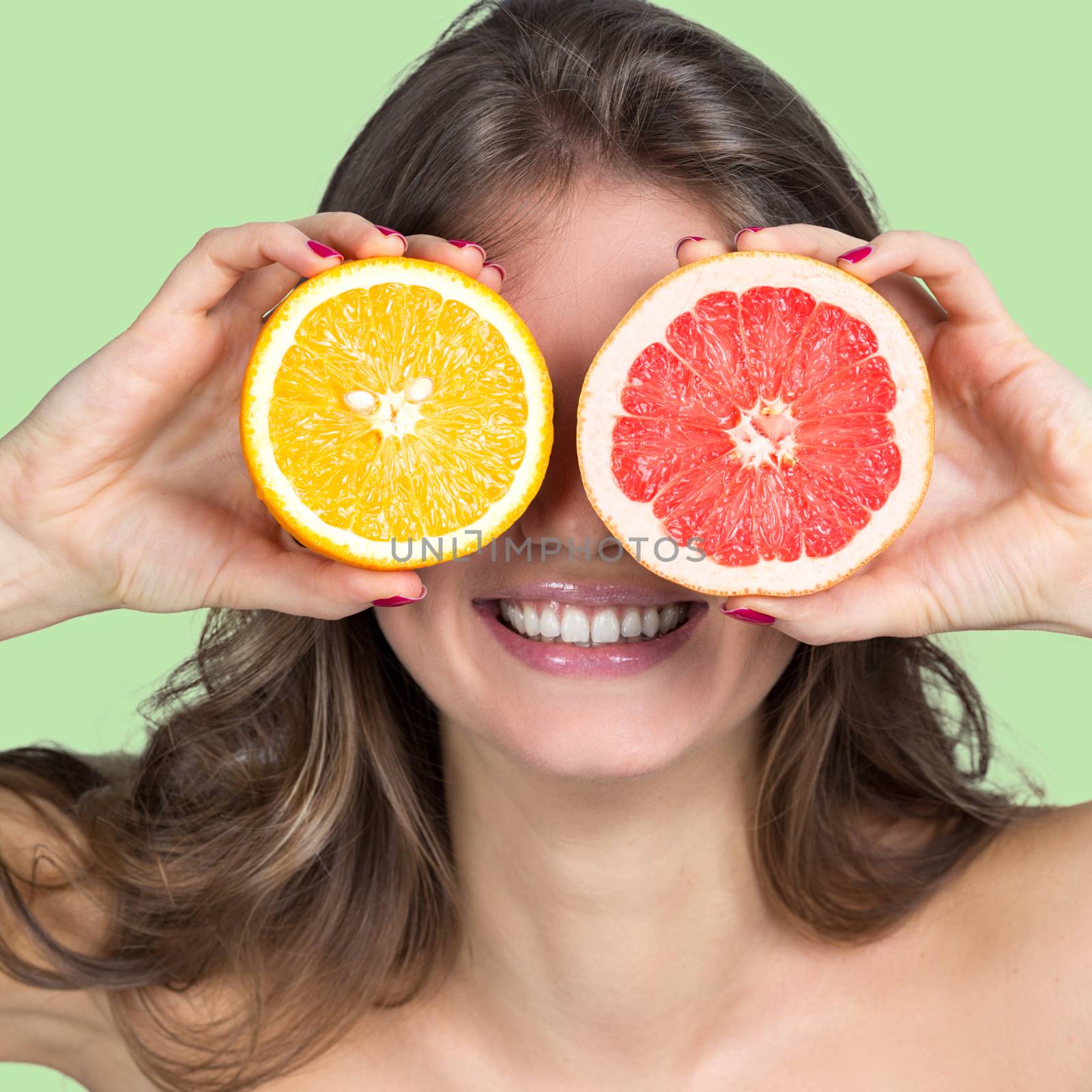 Smiling woman holding slices of orange and grapefruit in front of her eyes