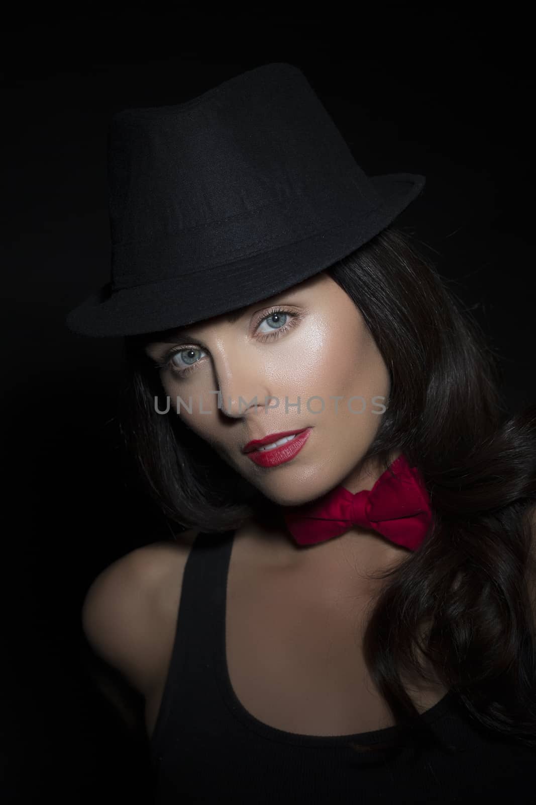 Portrait of beautiful young woman wearing tophat and bow-tie on black background