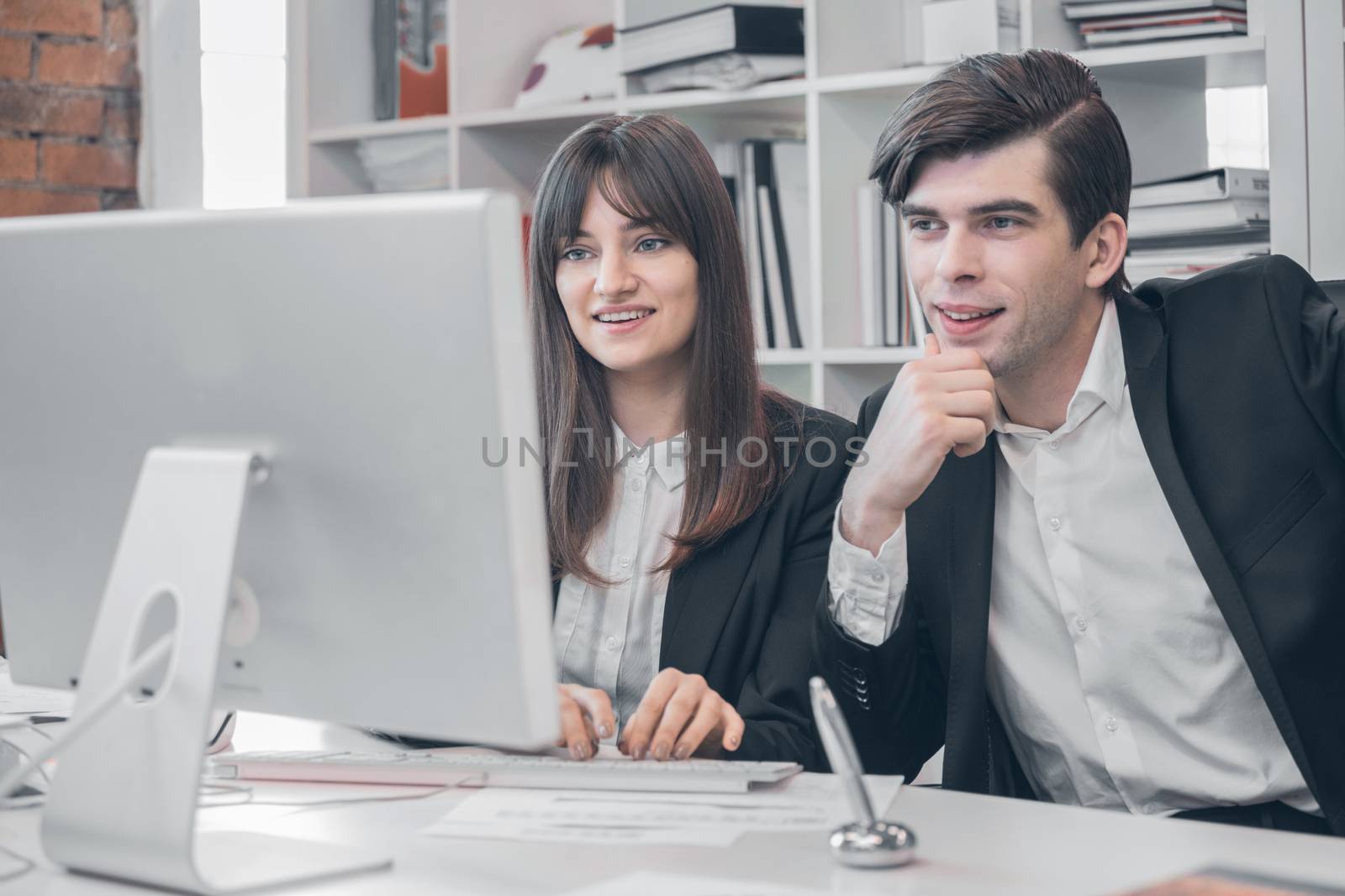 Two business people at monitor of desktop computer in office