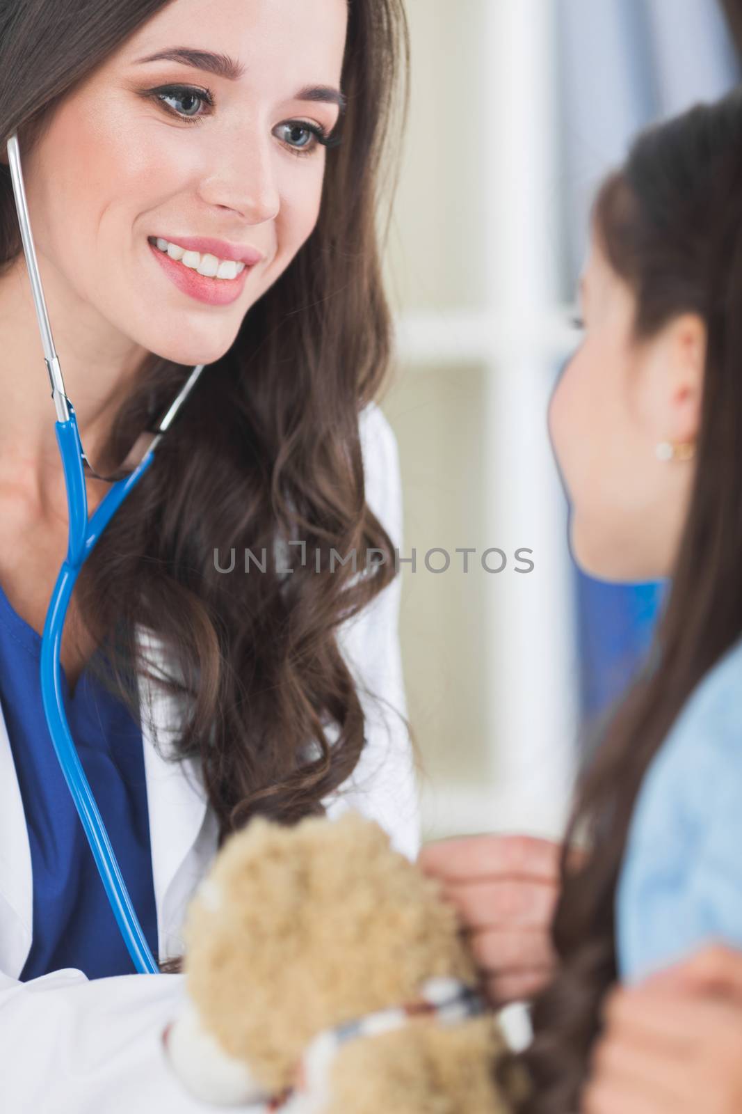 Beautiful female pediatrician doctor examining child with teddy bear in office