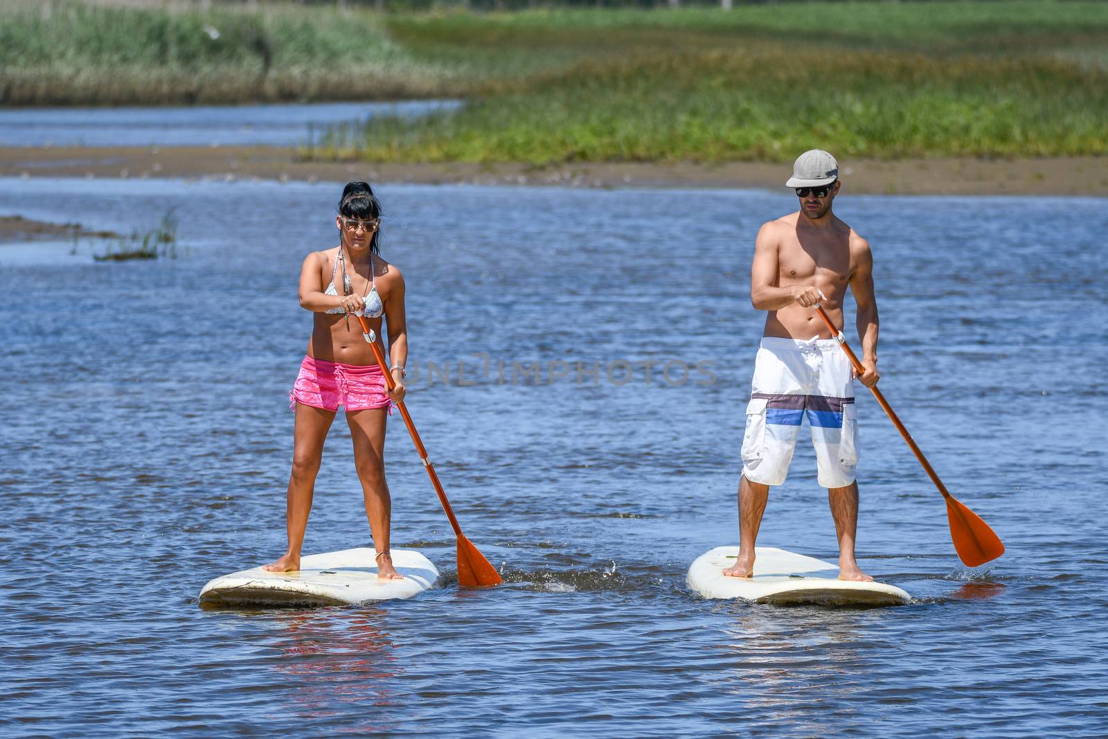 Man and woman stand up paddleboarding by homydesign