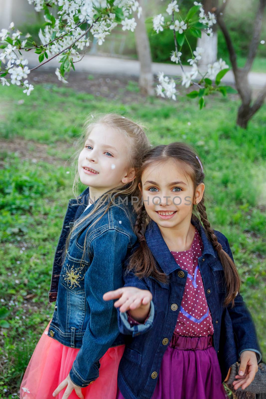 Two happy girls enjoying falling petals in spring garden