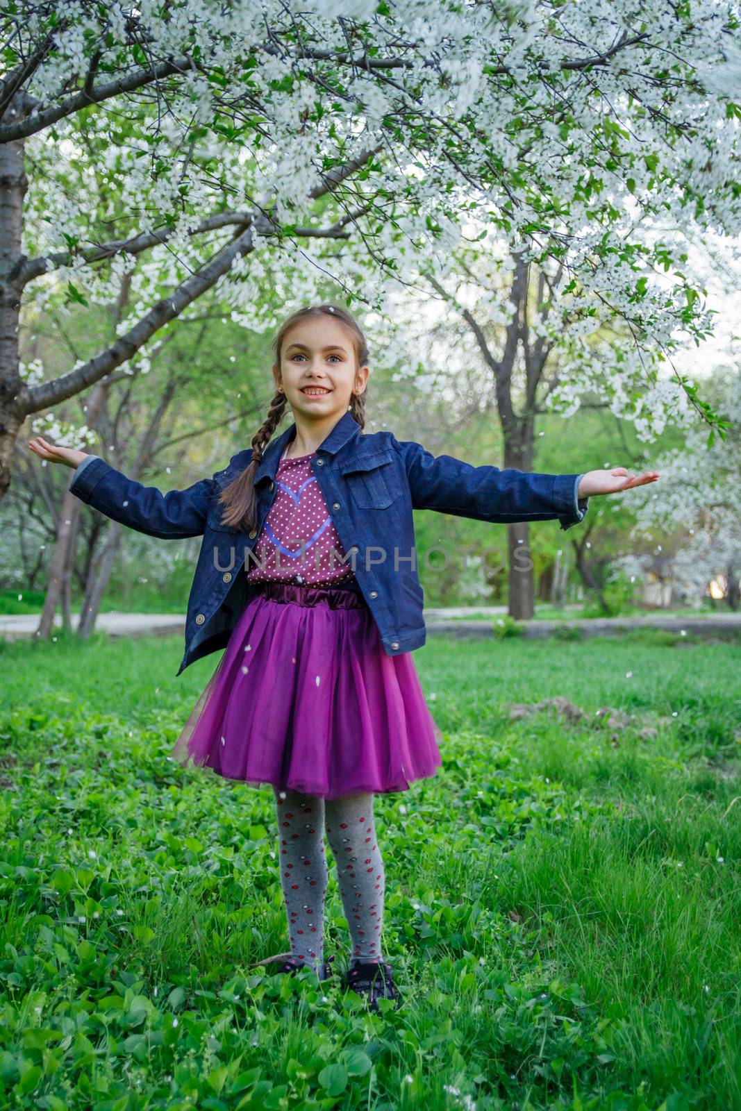 Smiling girl enjoying falling petals among spring garden