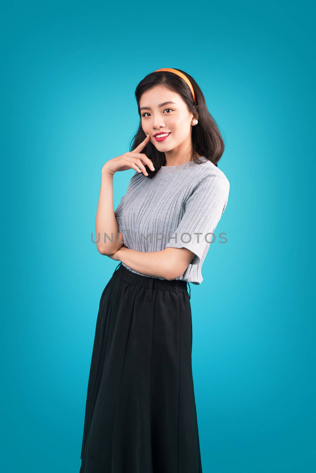 Smiling lovely asian woman dressed in pin-up style dress over blue.