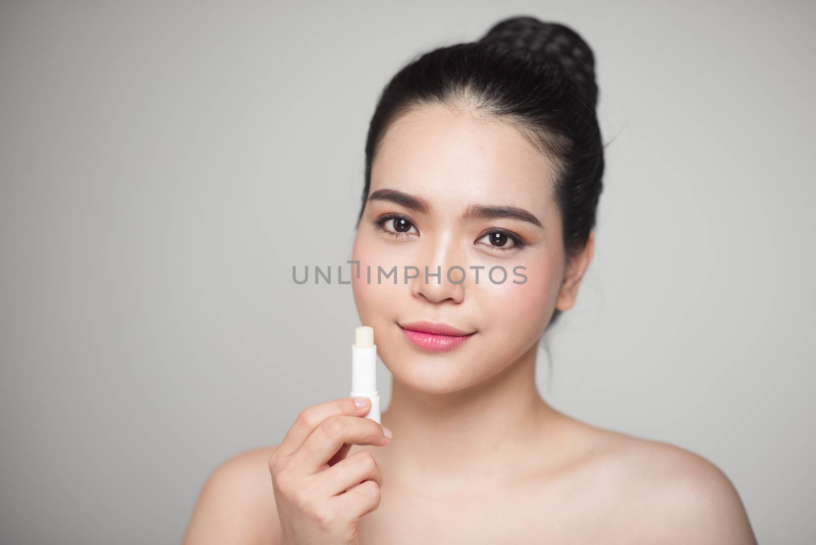Asian woman applying hygienic lip balm over grey background by makidotvn