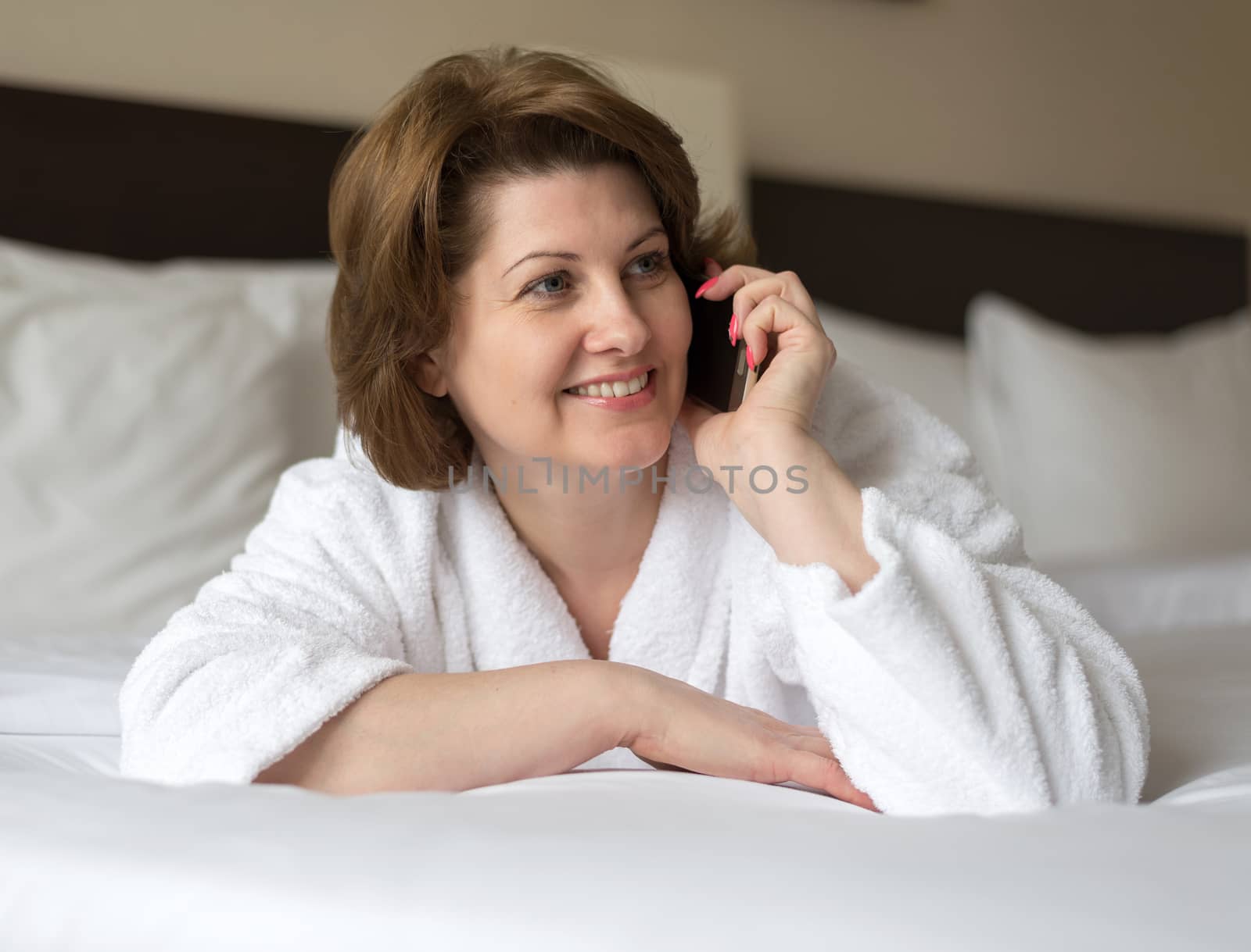 Woman in bathrobe talking on phone in hotel room by olgavolodina