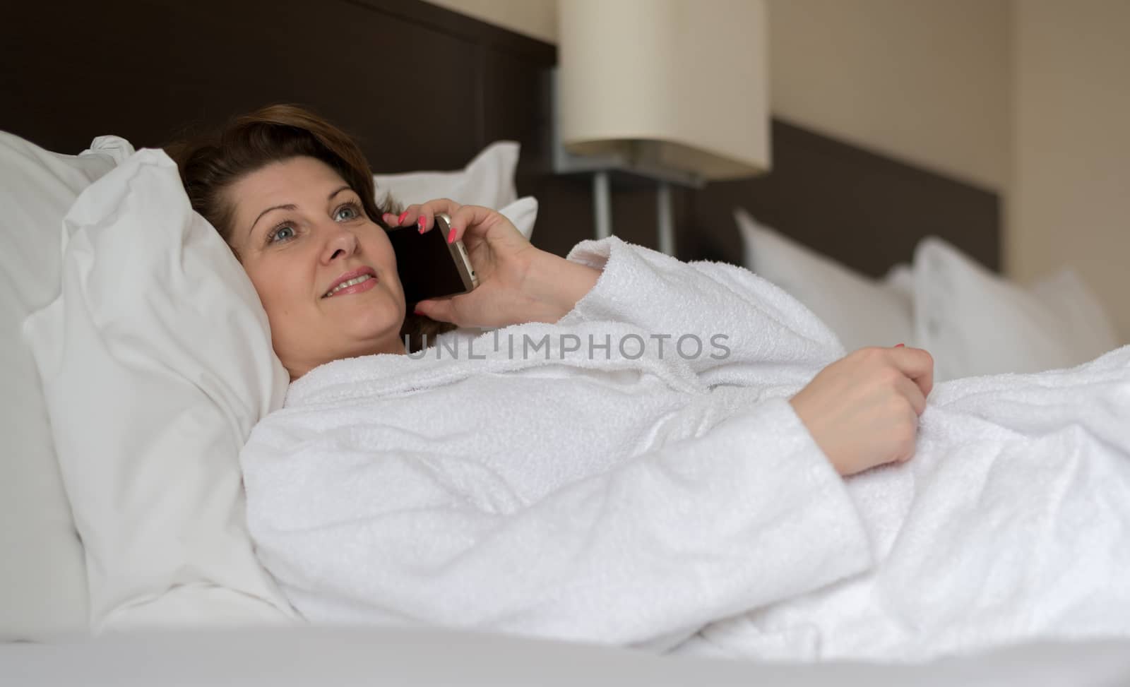 Woman in bathrobe talking on phone in hotel room by olgavolodina