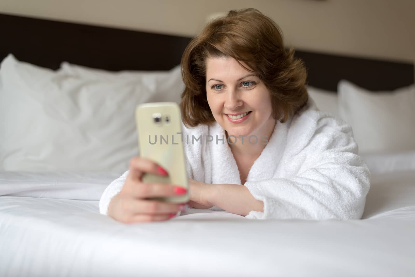 A woman in bathrobe wears telephone in hotel room by olgavolodina