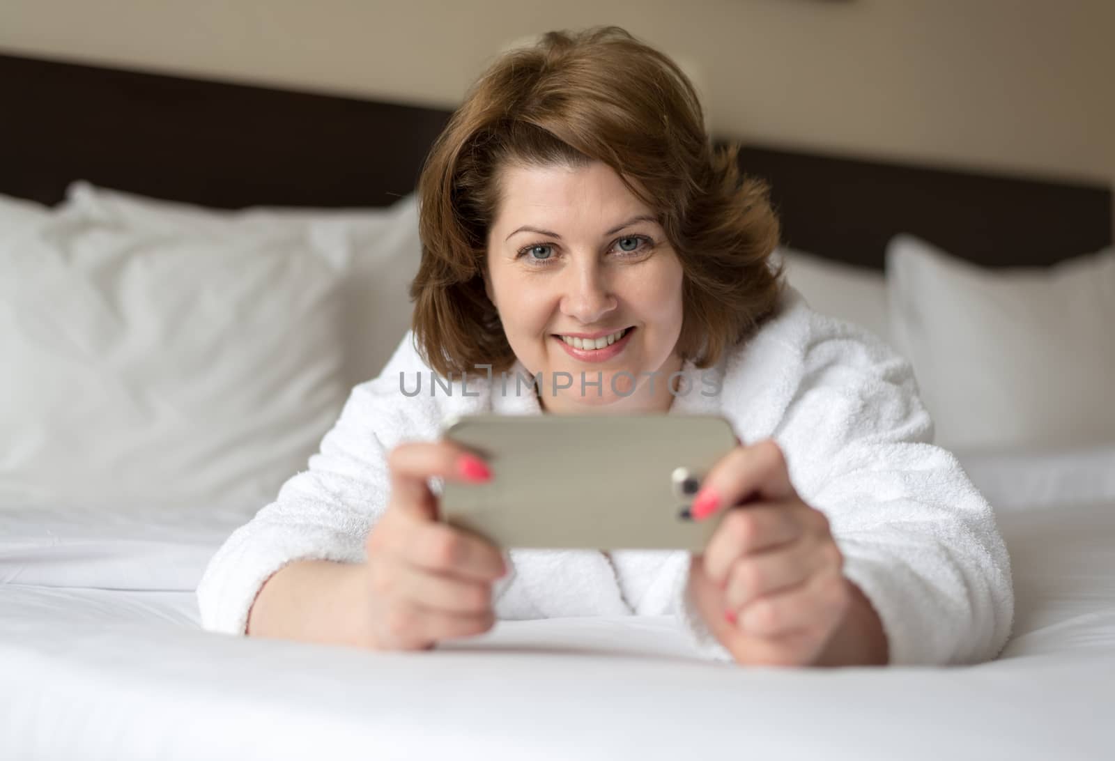 A woman in bathrobe wears telephone in hotel room by olgavolodina