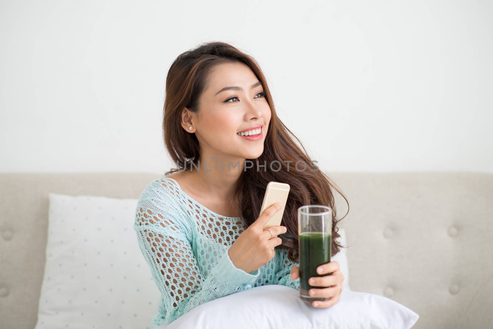 Asian woman using smartphone sitting on couch by makidotvn