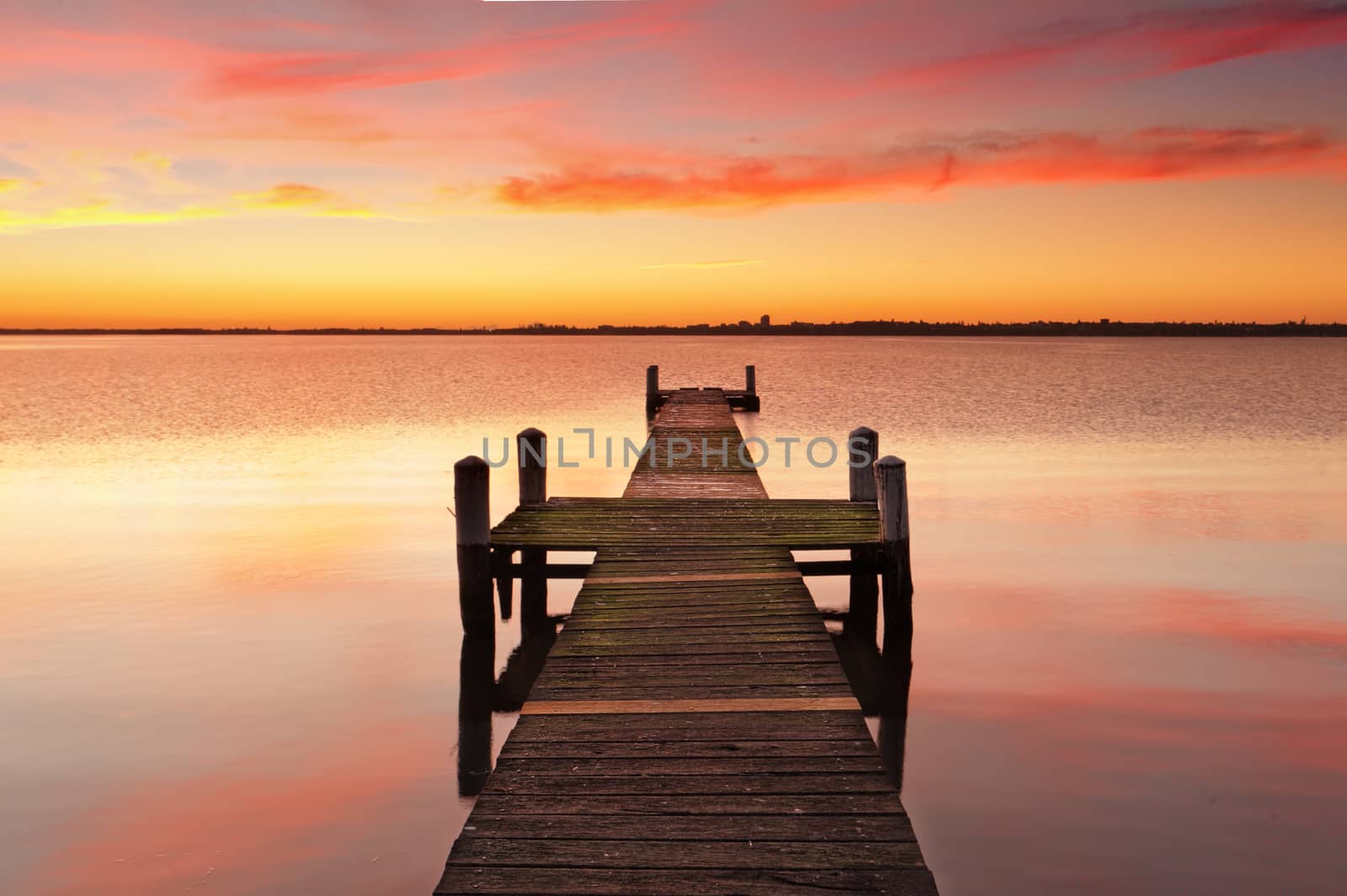 Stunning vivid red sunrise and timber jetty with reflections of the beautiful sky in the waters.  
Gorokan jetty, Australia