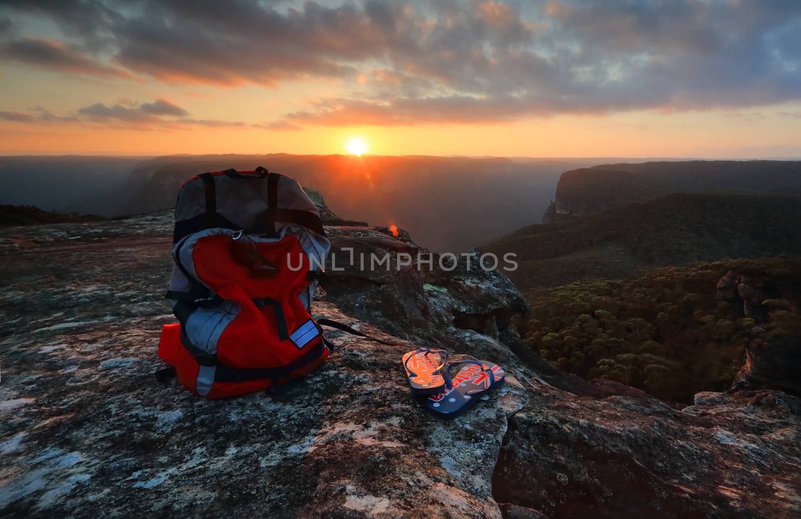 Sunset from a rocky outcrop of the Explorers Range, Blue Mountains Australia.  A  backpack and thongs with Australian flag sit catch the last light of the setting sun pver the Pierces Pass and Govets Gorge arm of the Grose Valley.