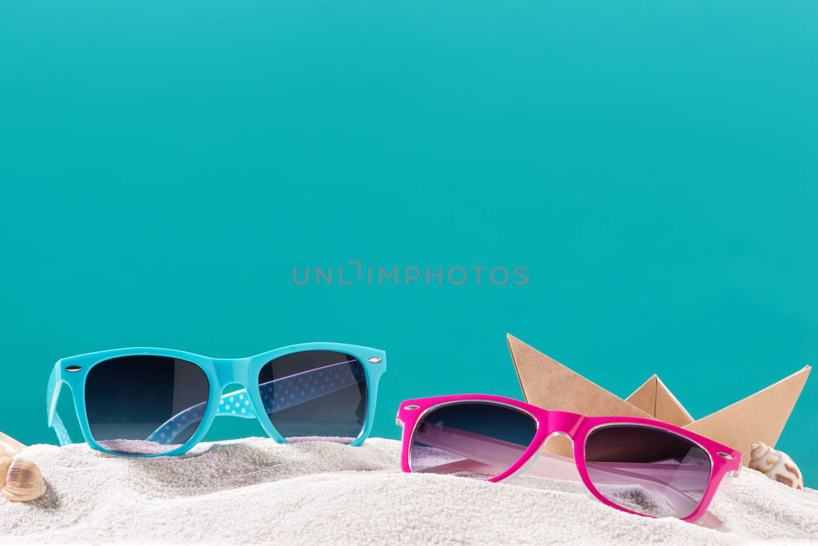 Row of colorful sunglasses on sand. by makidotvn