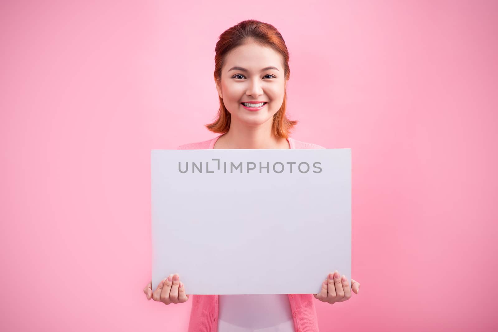 Cheerful beautiful asian young woman holding blank board on pink background.