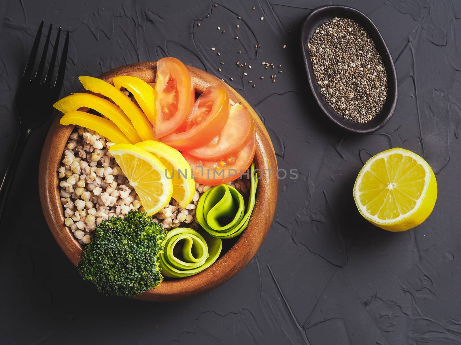 Top view of vegetarian buddha bowl with green buckwheat, broccoli, avocado, tomatoes and yellow sweet pepper paprika on dark concrete background with copy space