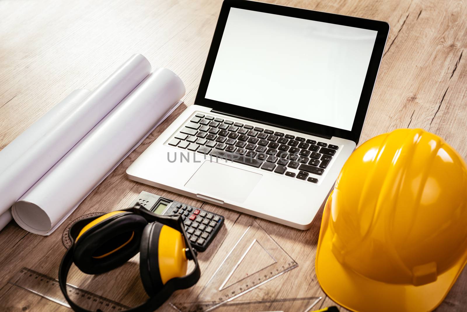 Top view of a architectonic workspace with laptop and yellow helmet. Different accessories, plans and cup of coffee is on the table. 