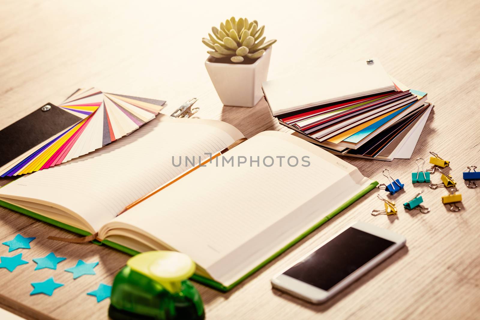 Designer workspace with blank notebook and pallete color. Different office accessories and smartphone is on the table. 