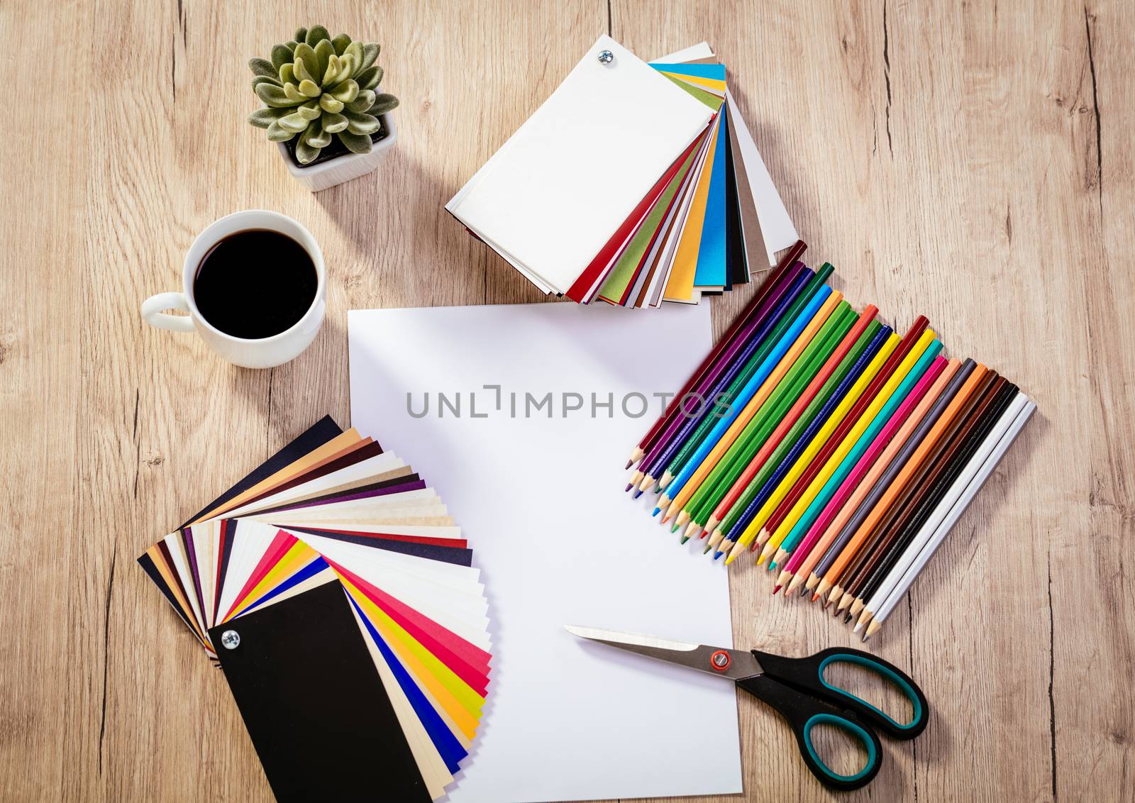 Top view of a designer workspace with blank paper and pallete color. Different office accessories and cup of coffee is on the table. 