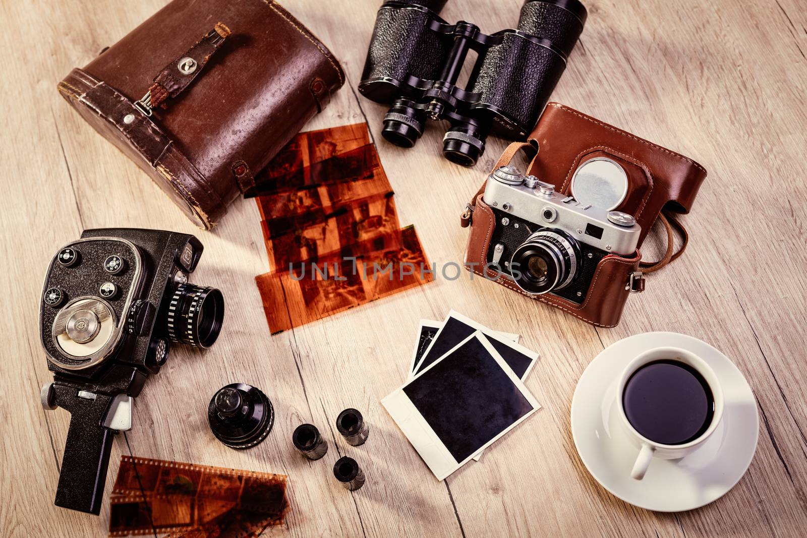 Top view of a old-fashioned cameras with films and lens. Next on table is retro binoculars and cup of coffee. 