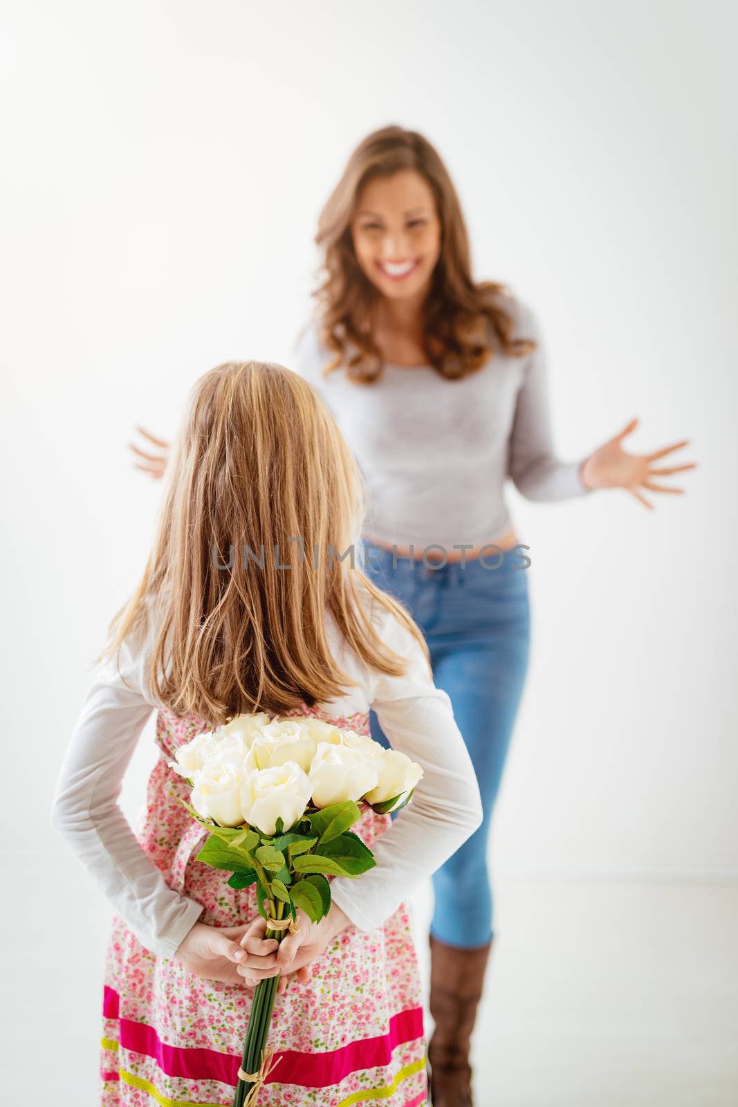 Cute daughter giving her mother bouquet white roses for Mother's Day. Selective focus. Focus on foreground, on little girl and flowers.