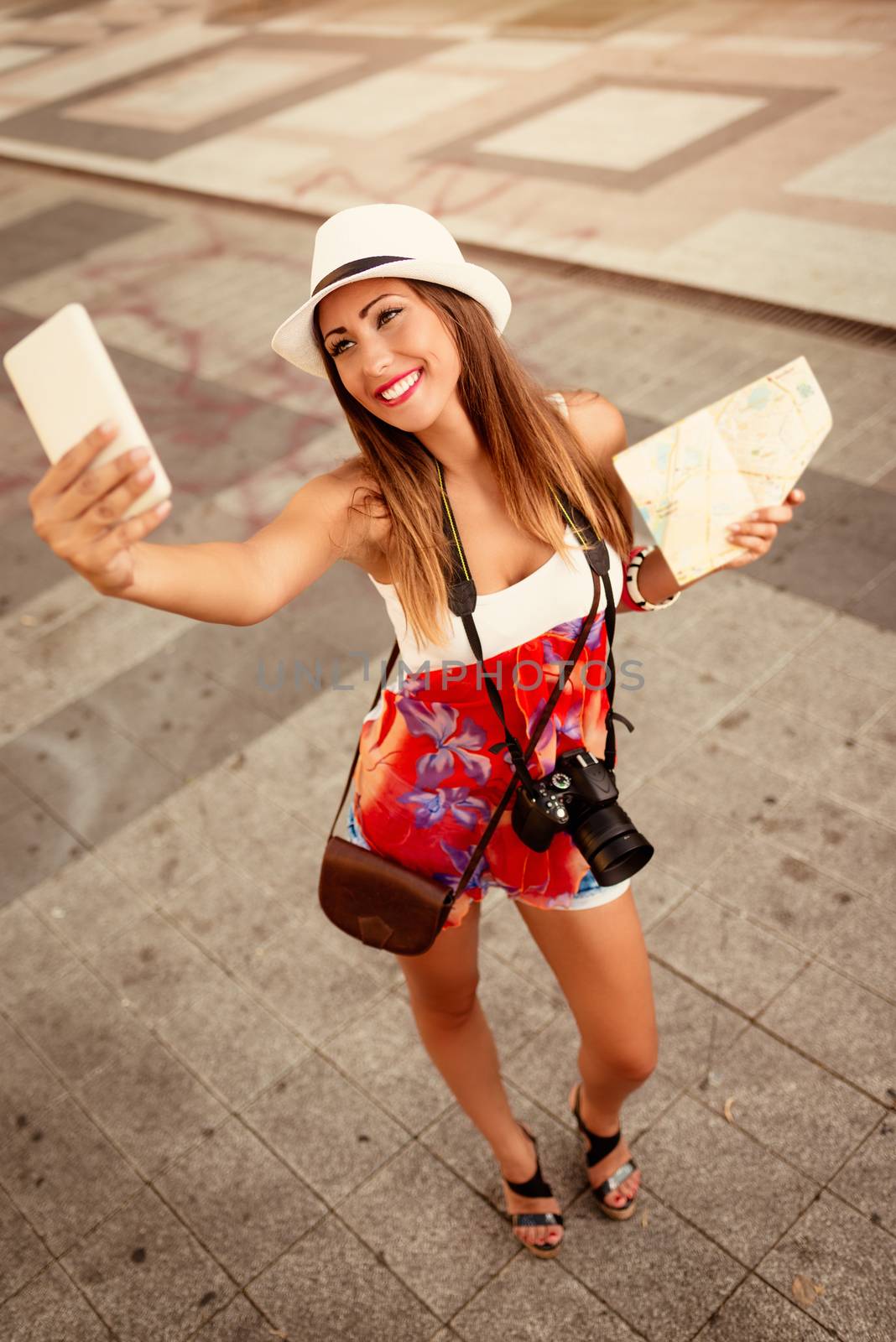 Beautiful tourist girl with hat holding map and taking selfie at the city square.