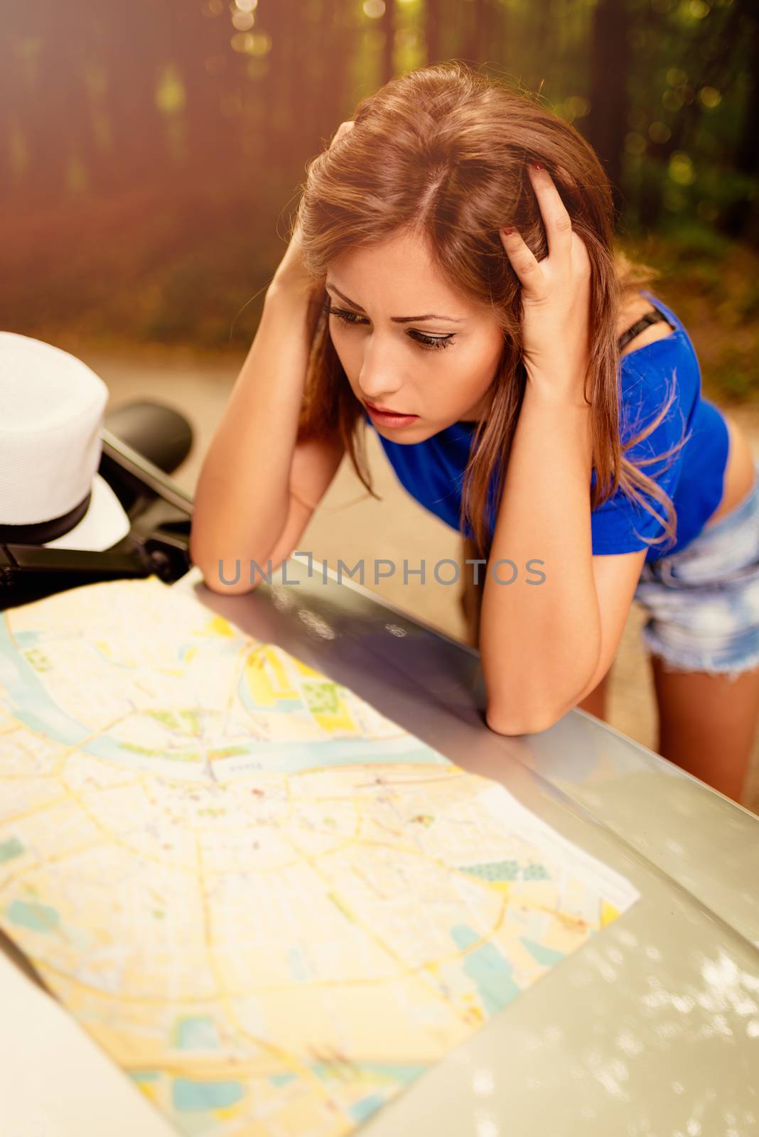 Confused lost beautiful woman standing leaning at car in the forest and worried looking a map.