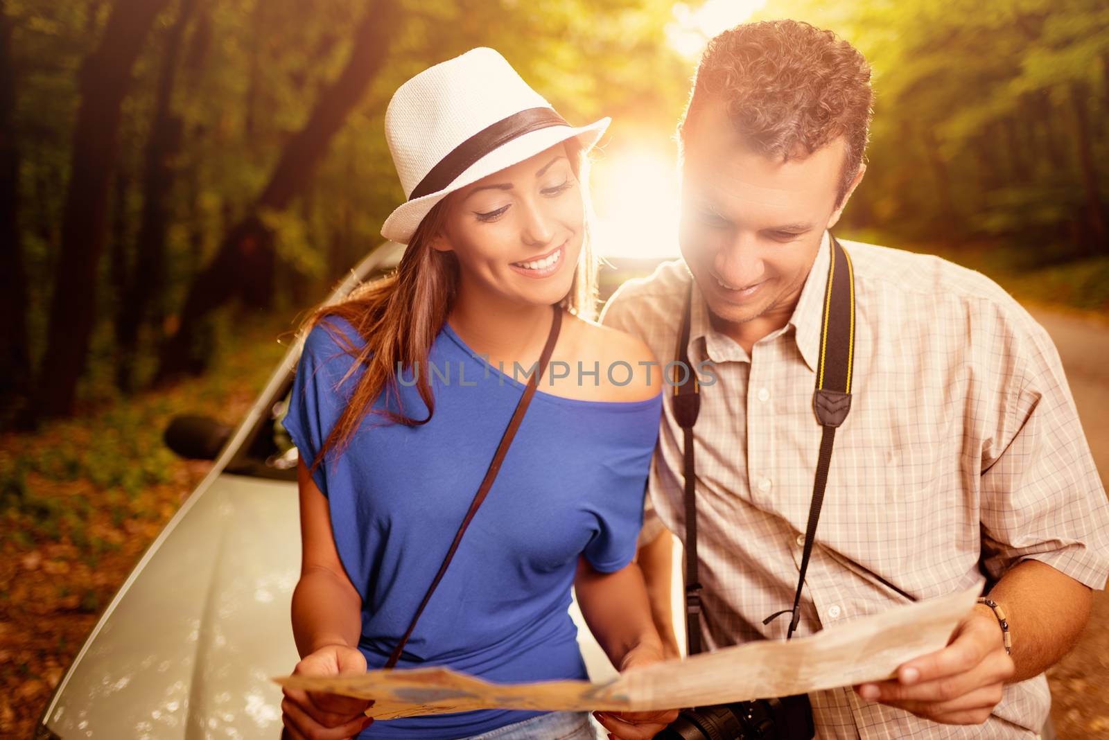 Young beautiful couple standing leaning at car in the forest and looking a map.