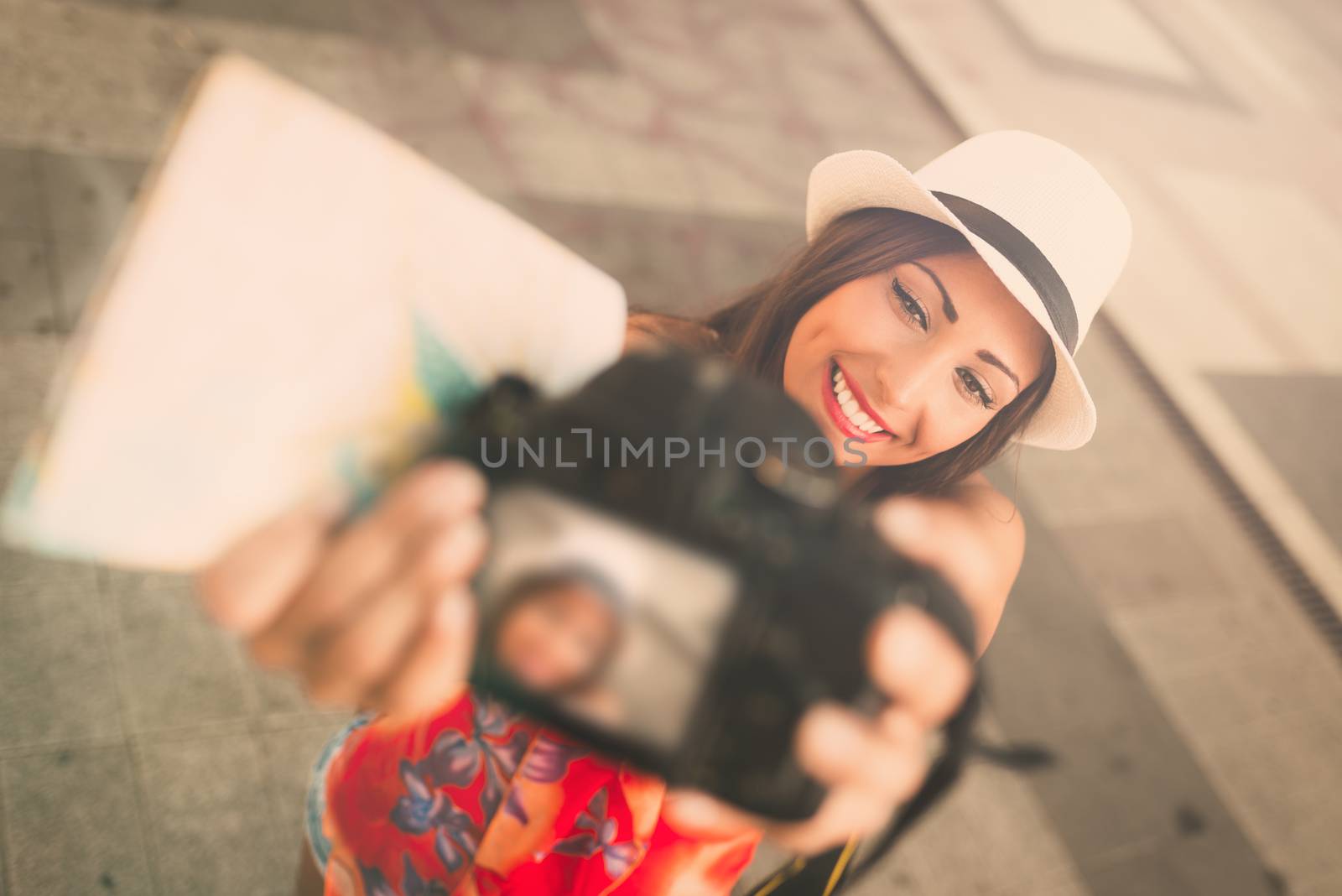 Beautiful tourist girl with hat holding map and taking selfie at the city square.
