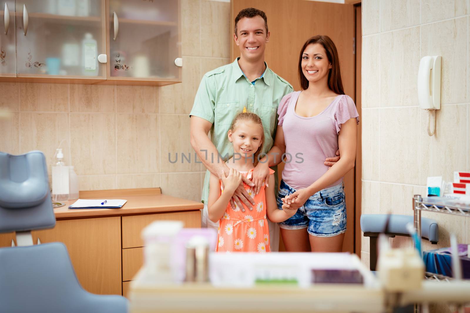 Happy young family at visit in the dentist office. They are standing and looking at camera.