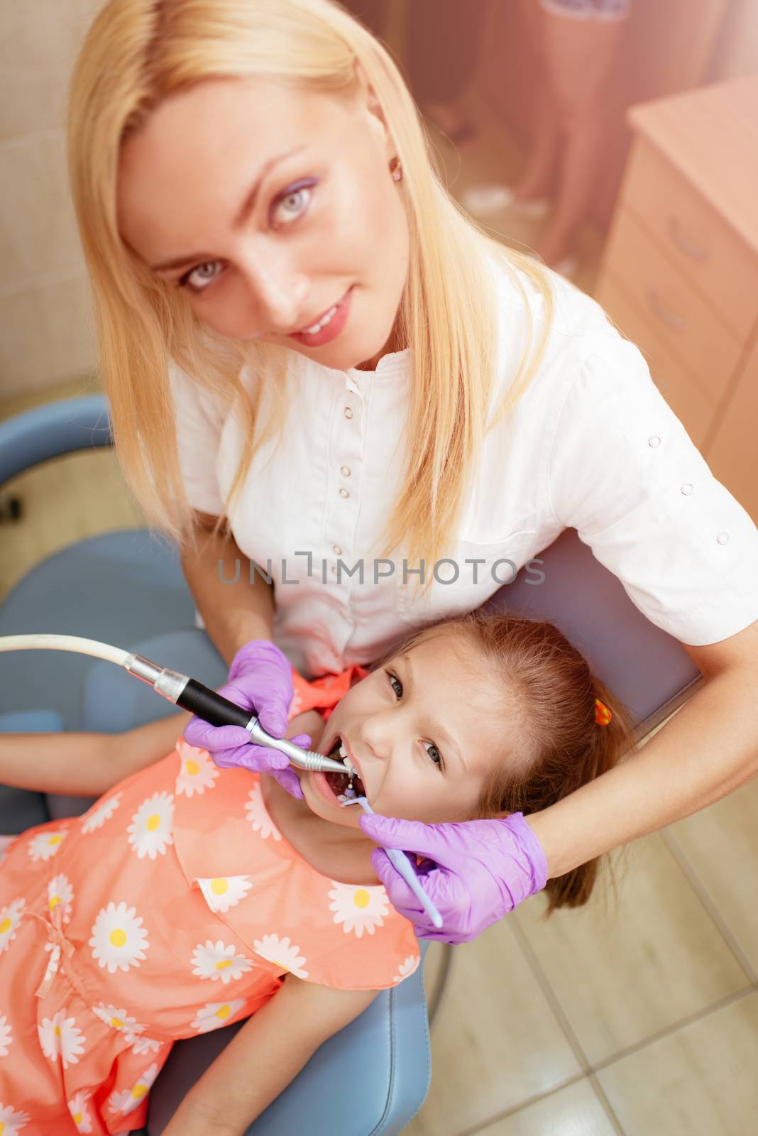 Beautiful little girl at visit in the dentist office. She is sitting on a chair and dentist polished teeth on her. Top view.