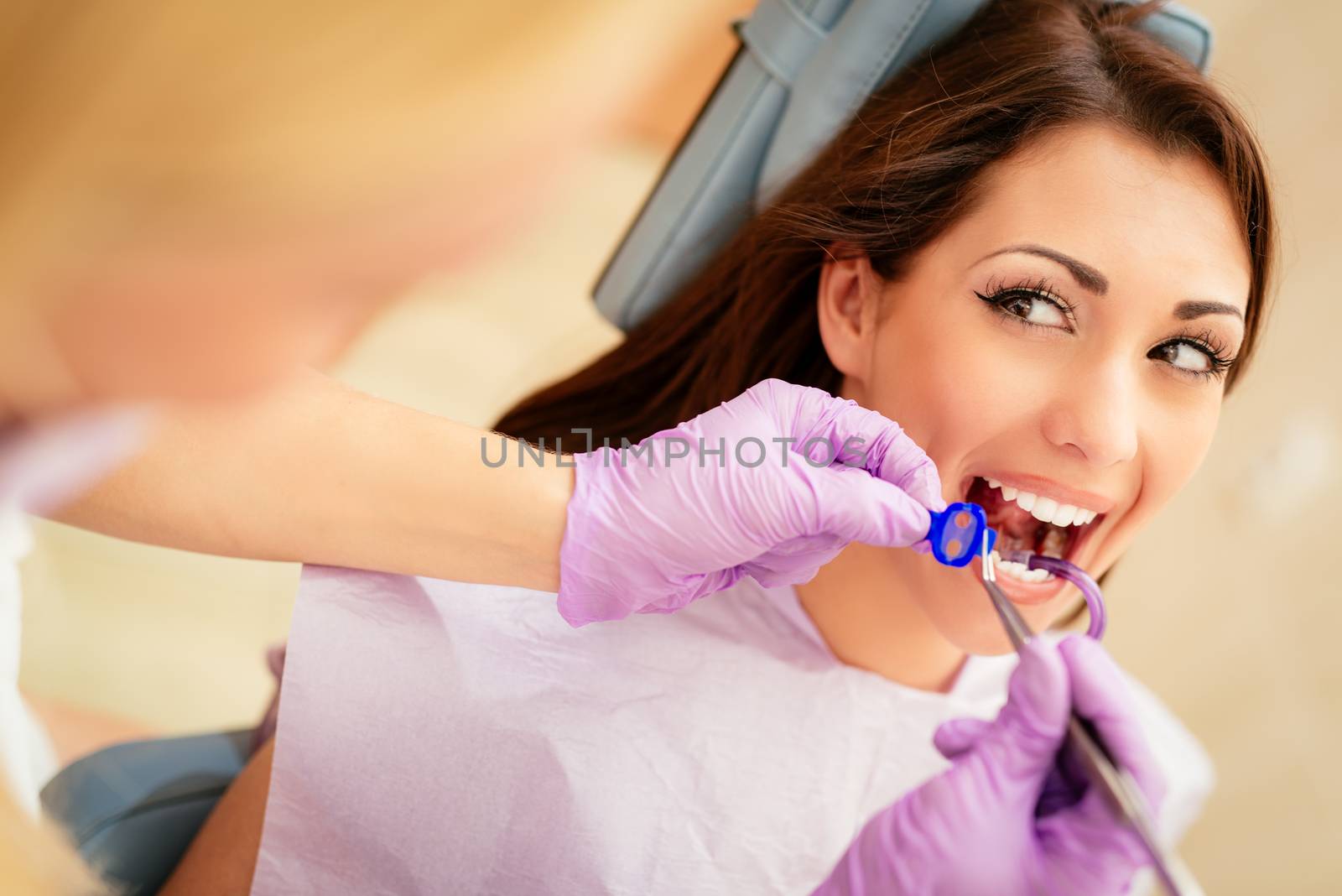 Beautiful young woman in visit at the dentist office. She is sitting on a chair and dentist repair teeth on her. Selective focus.