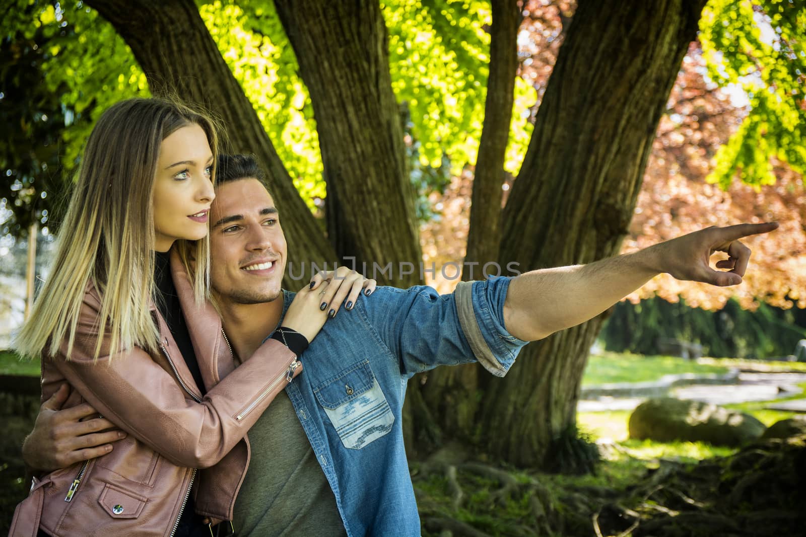 Boyfriend and girlfriend standing in countryside in green luscious field, embracing each other and cuddling, showing romantic love