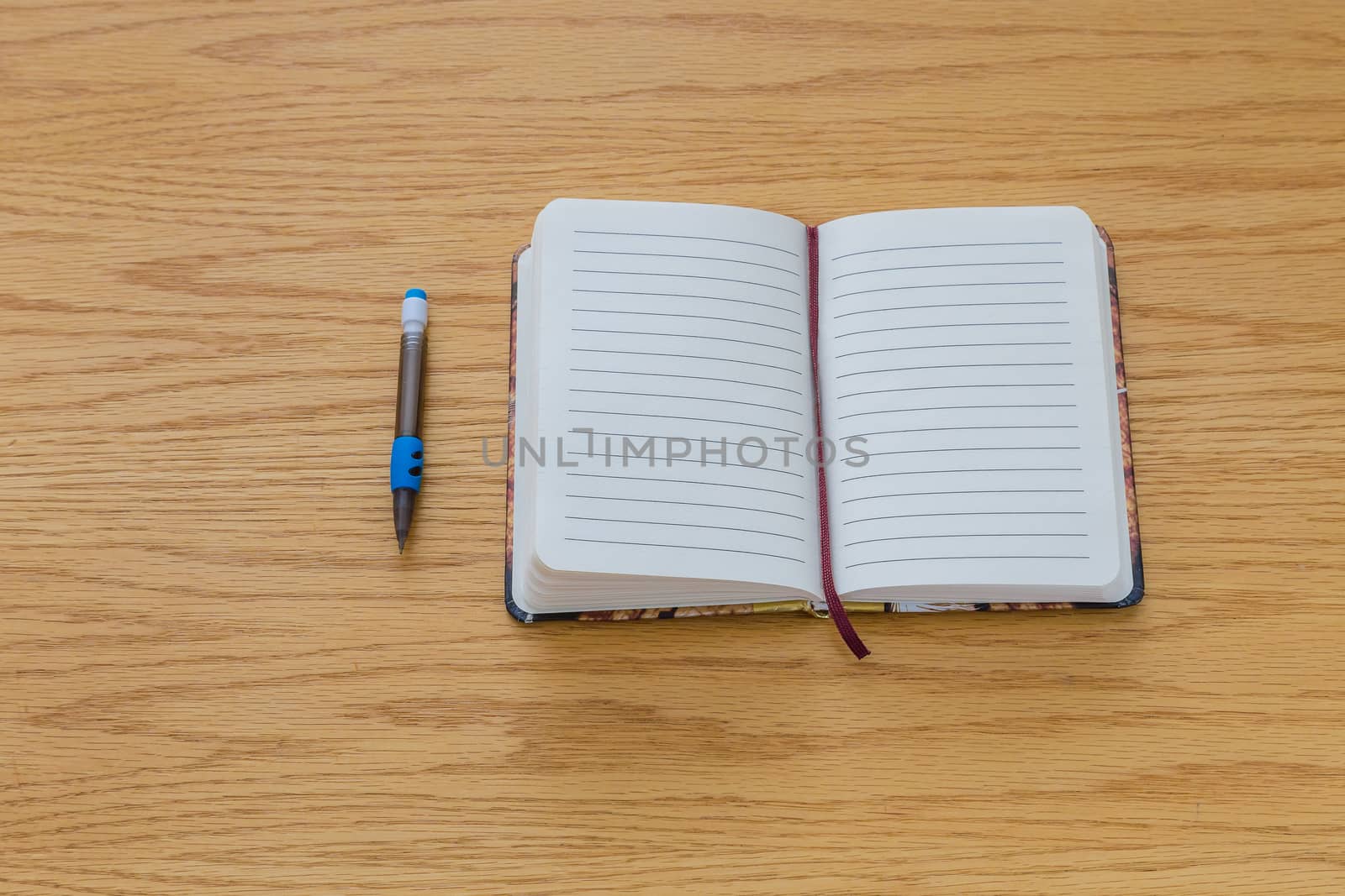 A pencile beside a notebook with blank pages on a table.