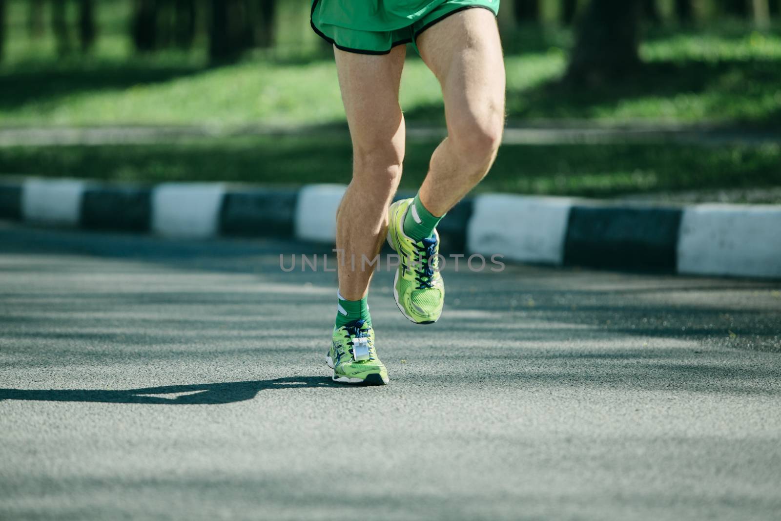 Marathon runner legs and green running sneakers of man jogging outdoors on asphalt road