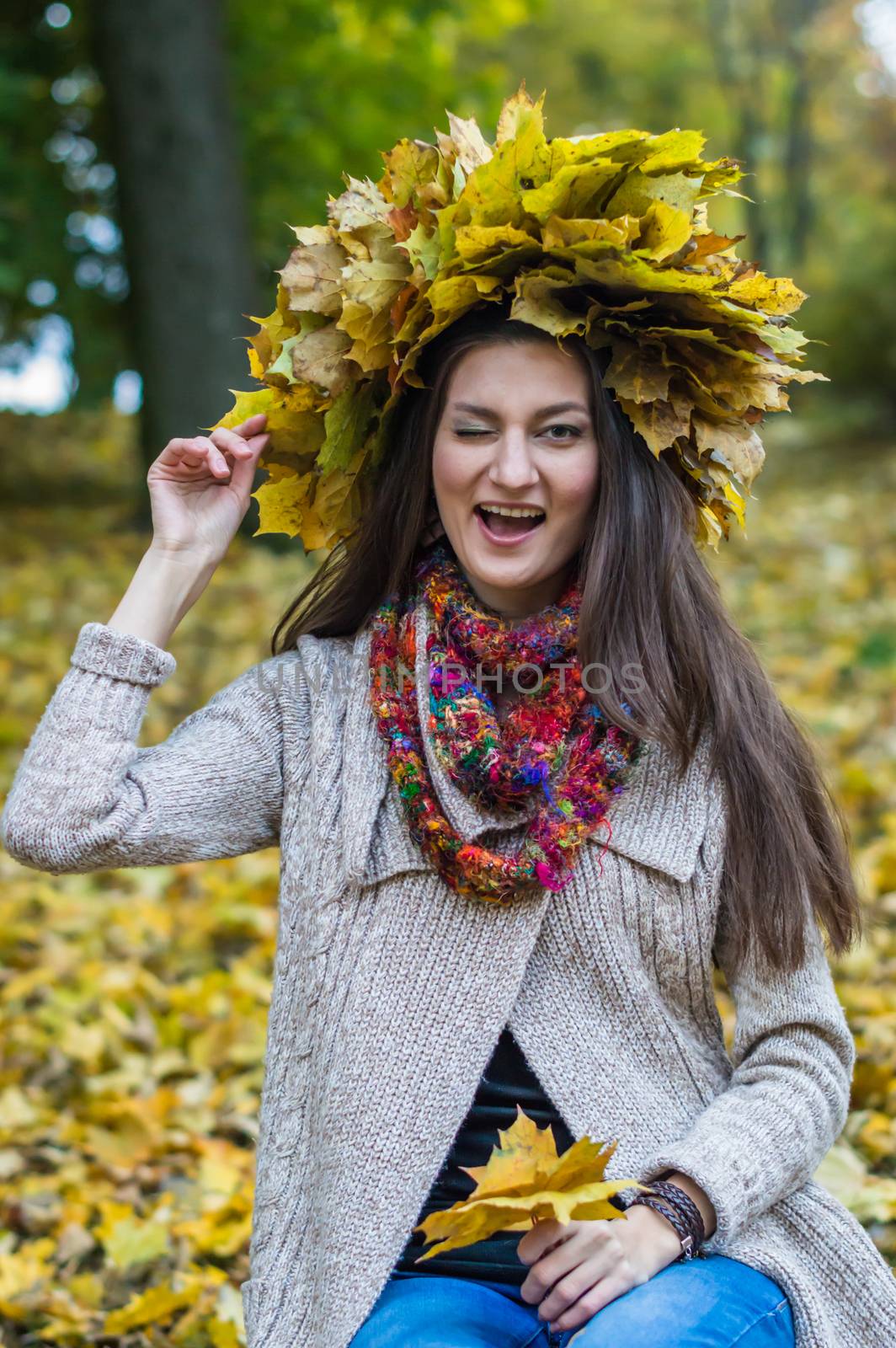 smiling, happy girl wearing a wreath of maple leaves in autumn park