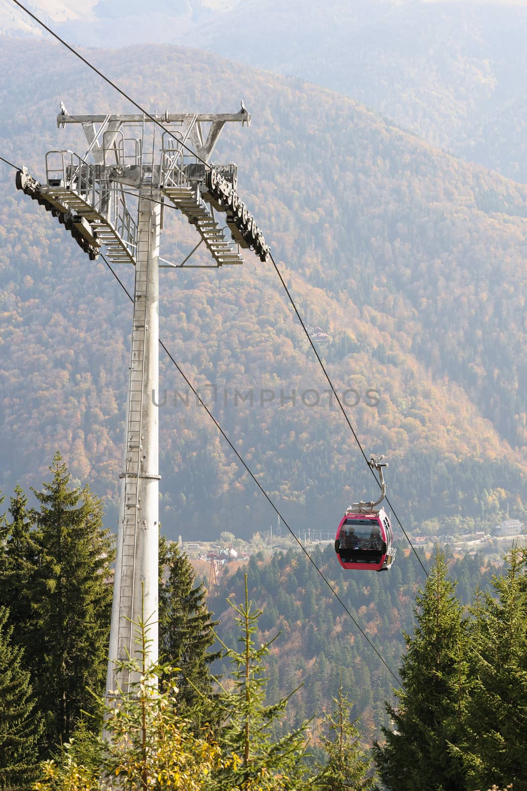 Cableway in Romanian Carpathians during summertime with passenger cabin moving. Focus at cabin, slightly blurred background