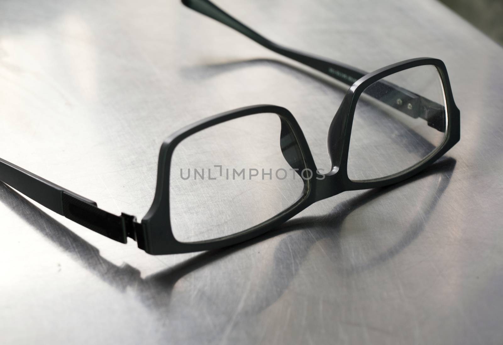 COLOR PHOTO OF PLASTIC FRAME GLASSES ON STEEL TABLE