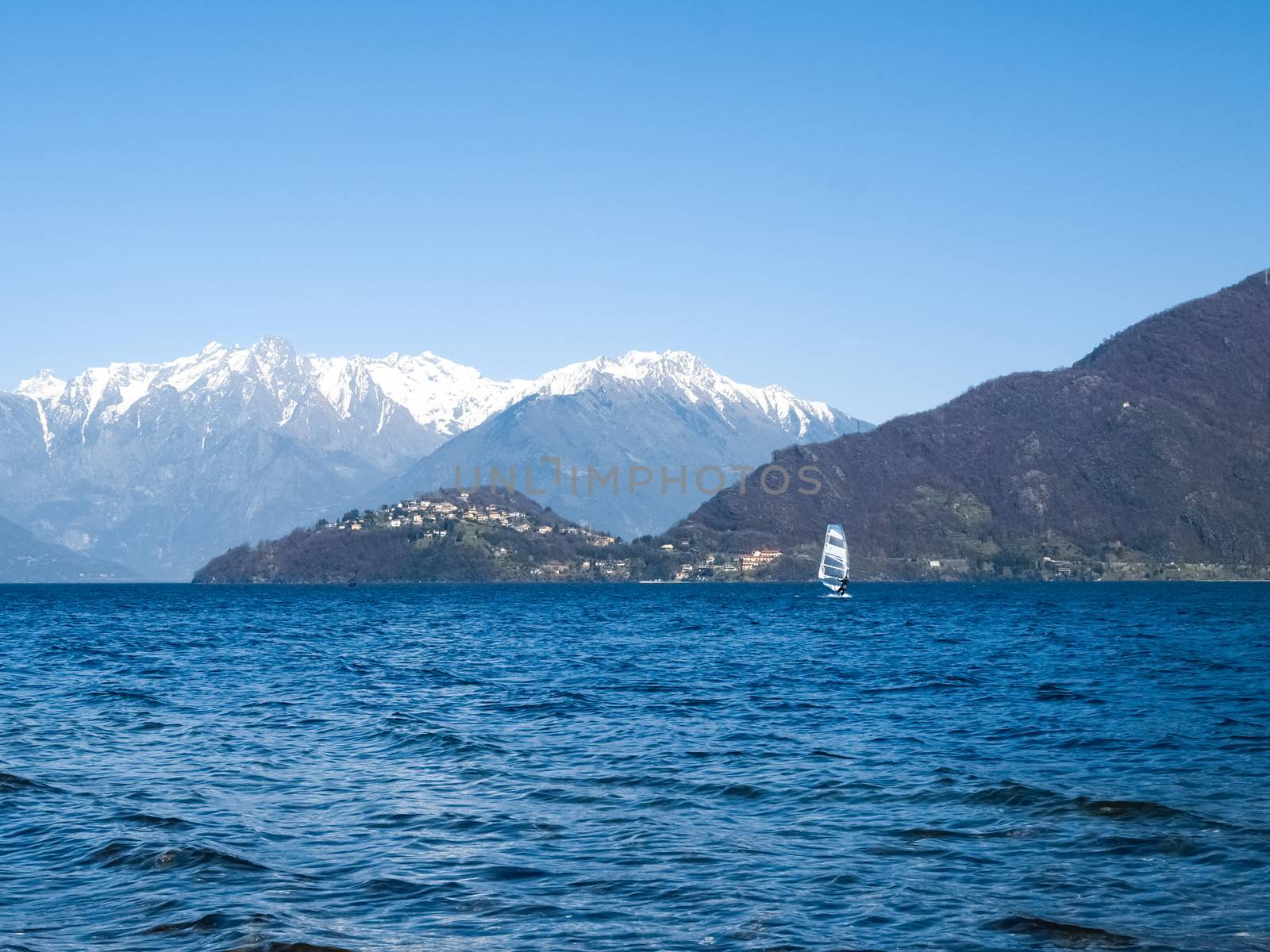 Pianello del Lario, Como - Italy: Windsurfer sailing on the lake and in the background you can see the peninsula of Piona and mountains