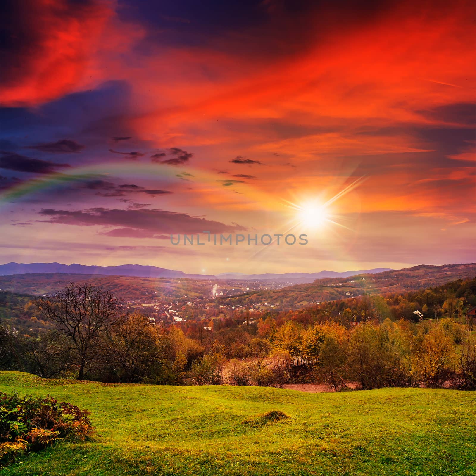 autumn landscape. village on the hillside. forest on the mountain light fall on clearing on mountains with rainbow in evening light