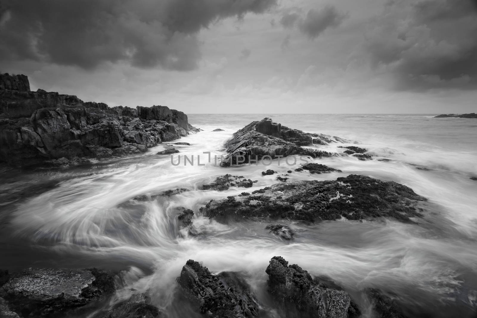 Seascape at low tide with moody clouds and pending storms and swirling ocean currents around the exposed rocks.