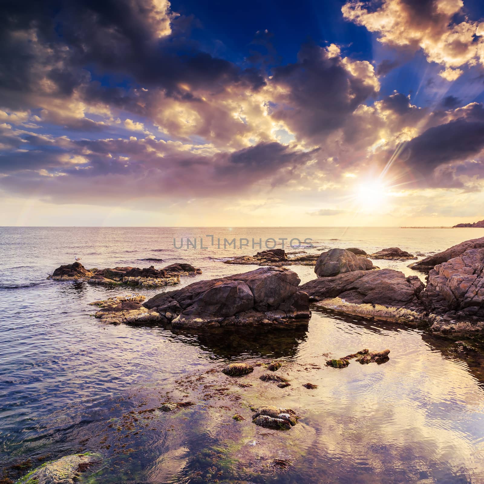 sea wave attacks the boulders and is broken about them at sunset