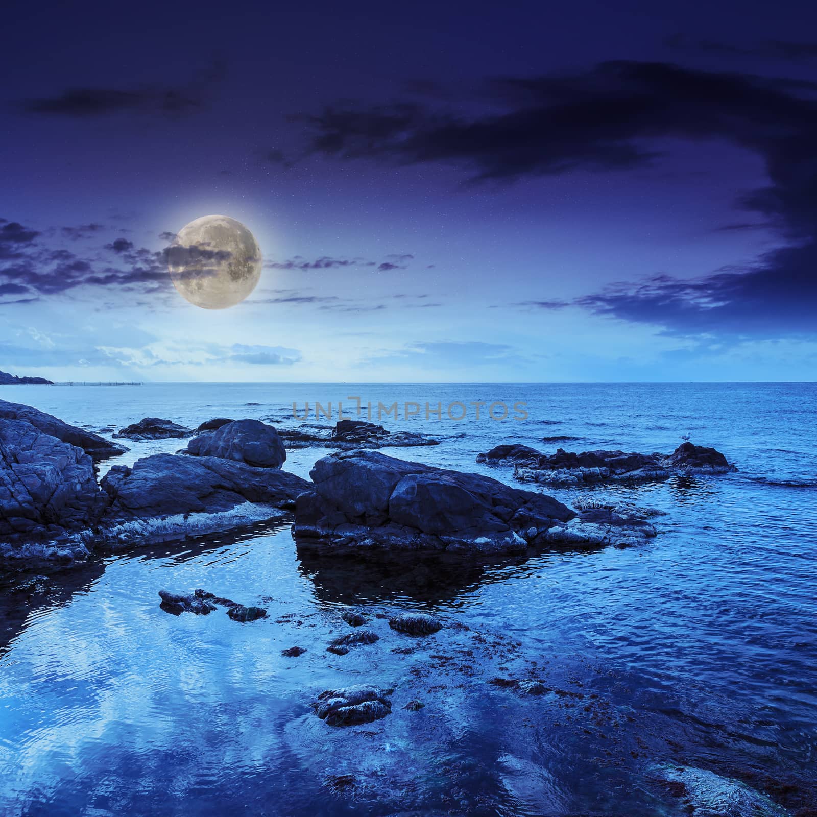 sea wave attacks the boulders and is broken about them at night in moon light