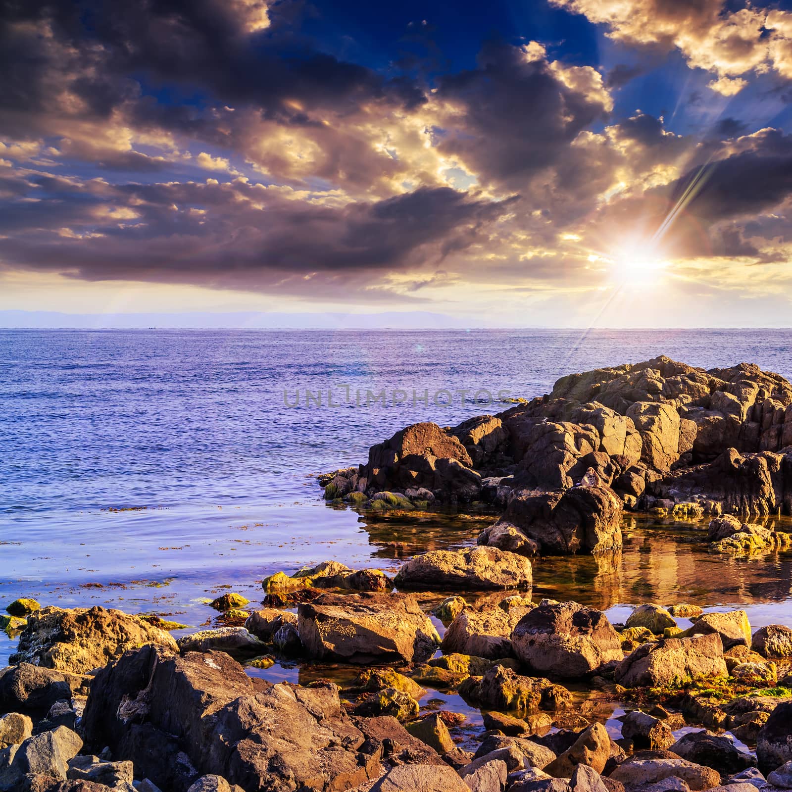 sea wave breaks about boulders at sunset by Pellinni