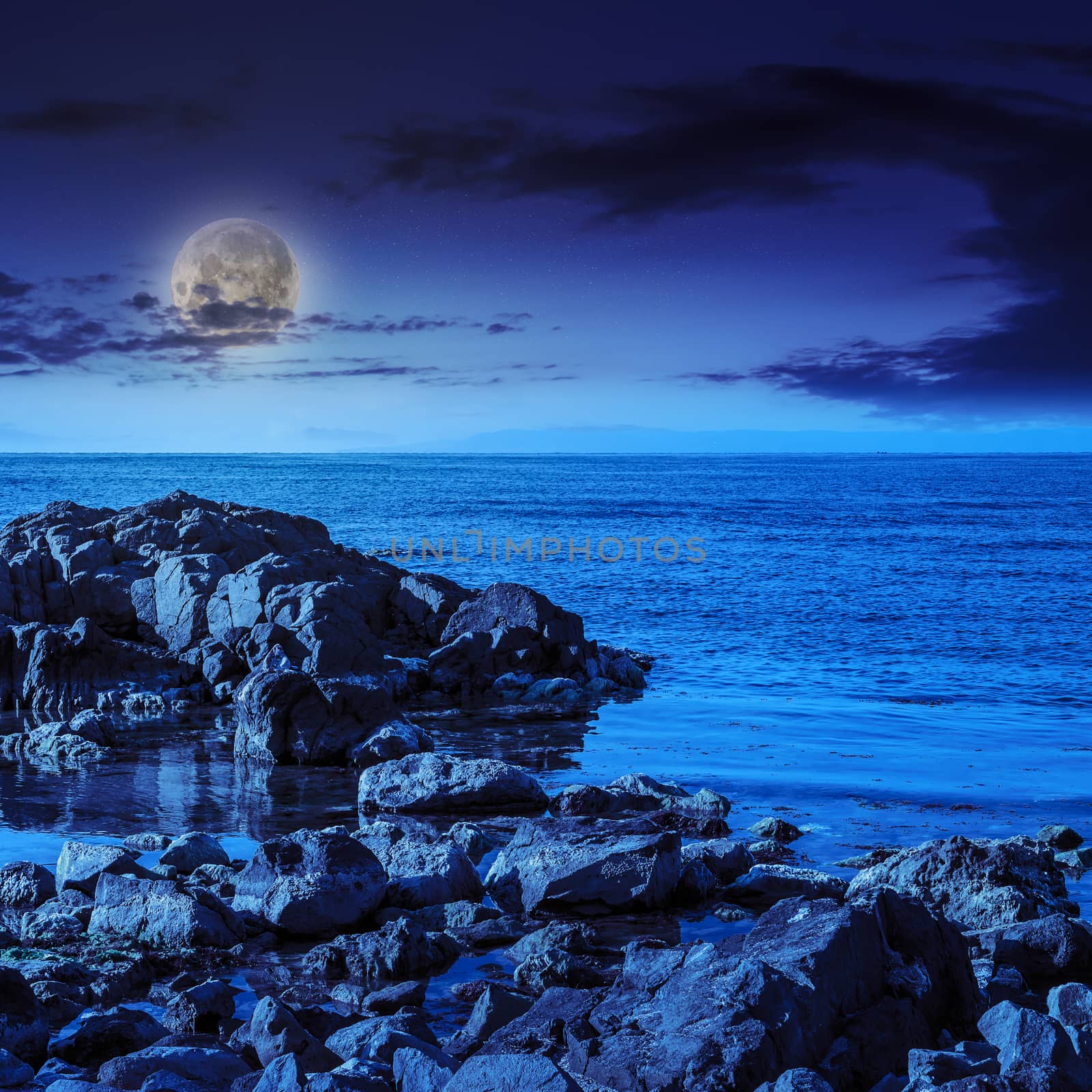 sea wave attacks the boulders and is broken about them at night in moon light