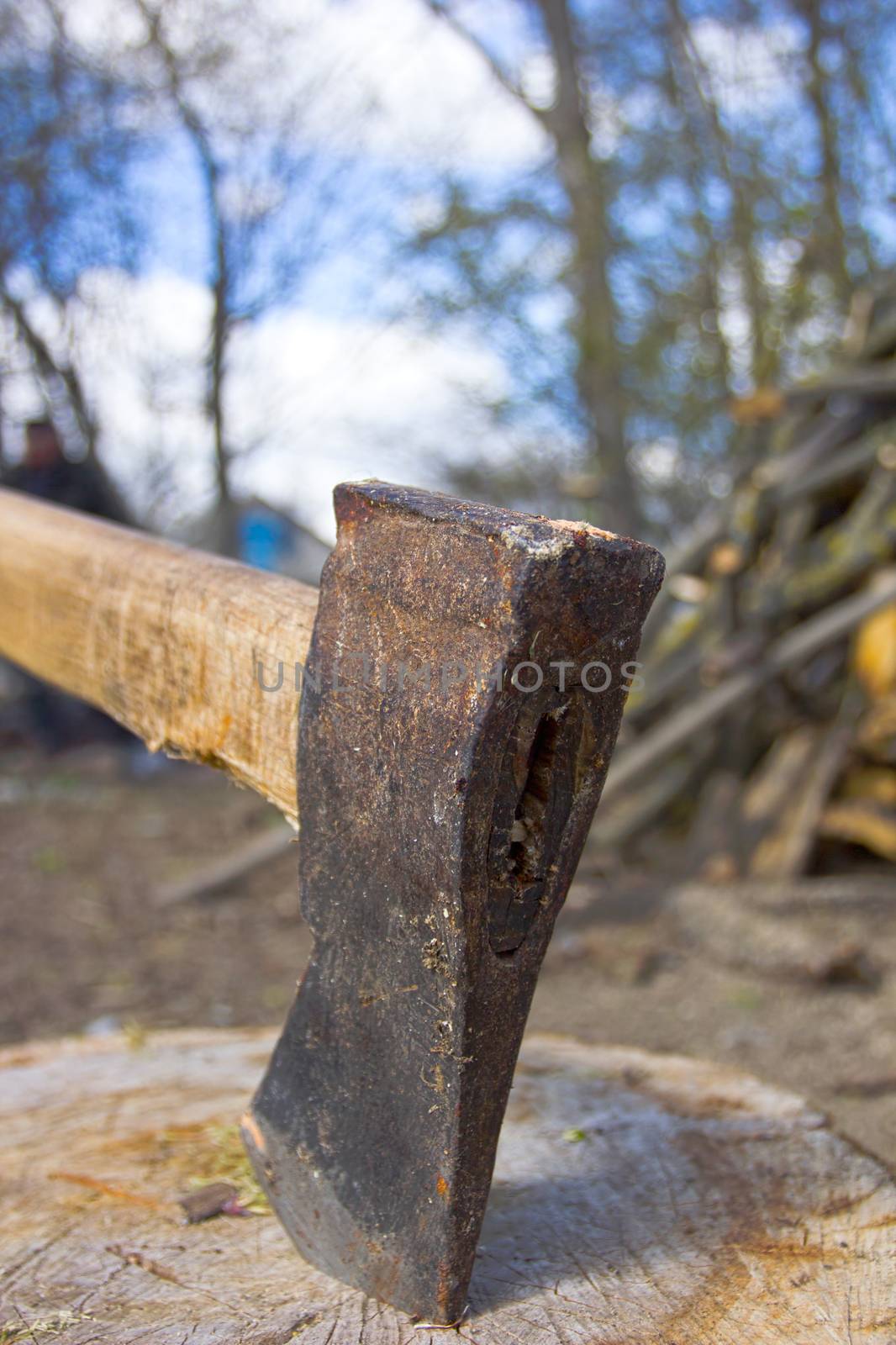 Close up shot of an axe in a stump with firewood in the background.